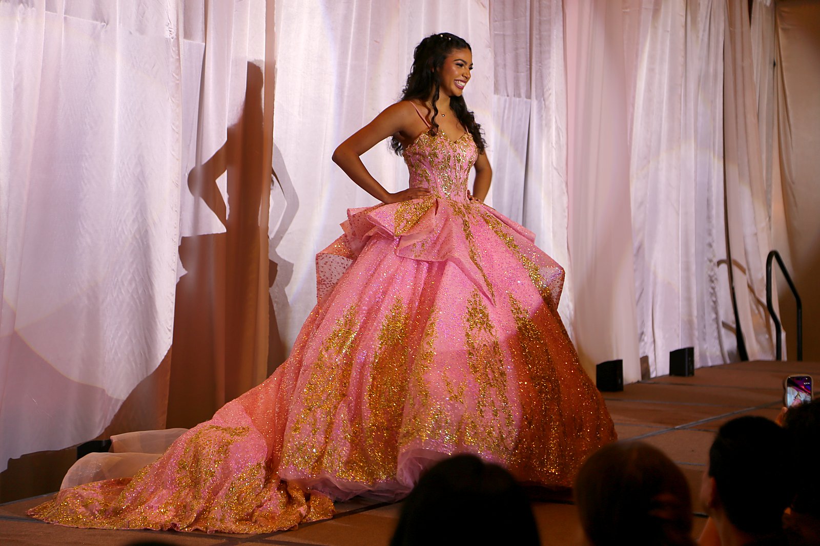 Model in a pink and gold quinceanera ball gown with half-up curled hair