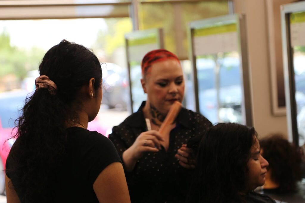 Lexie Cochran holds up a comb as they demonstrate to a student artist at a salon station.