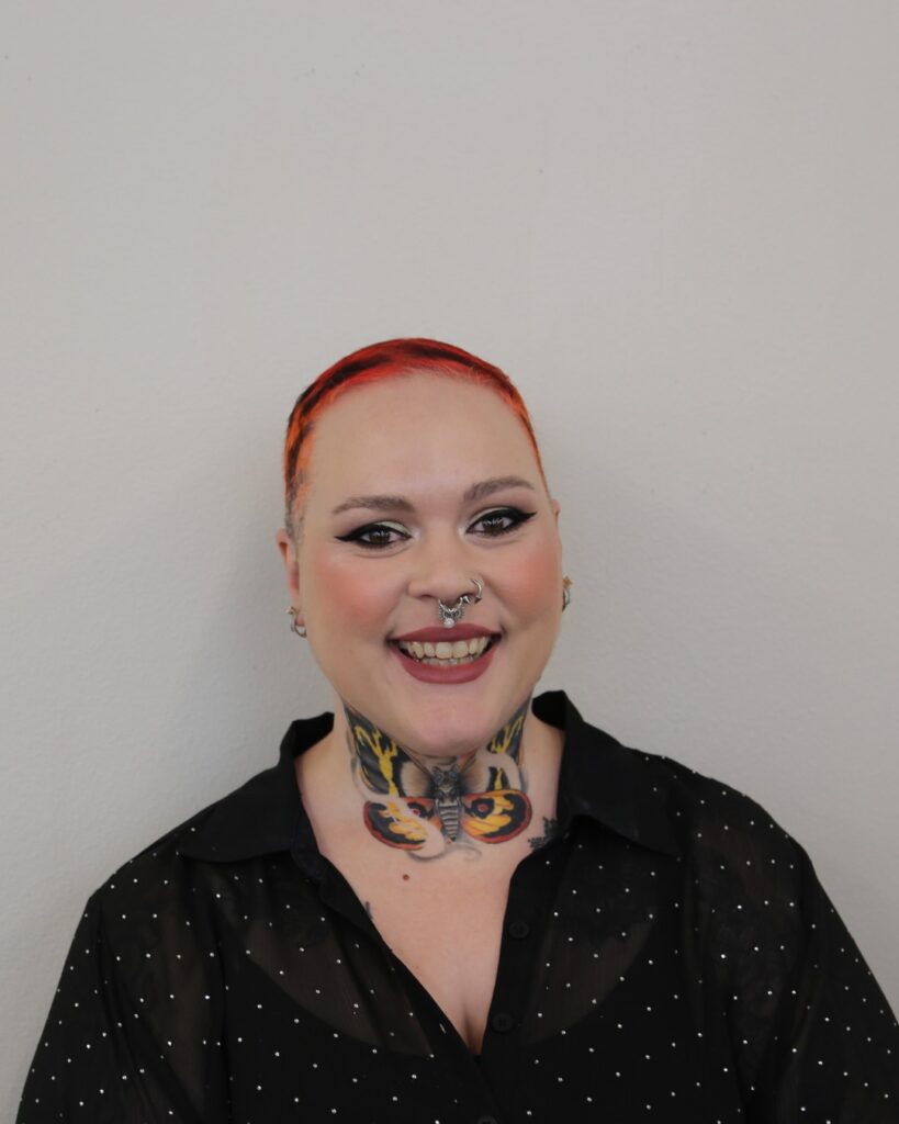Portrait of Lexie Cochran smiling against a gray wall, wearing a black patterned top.